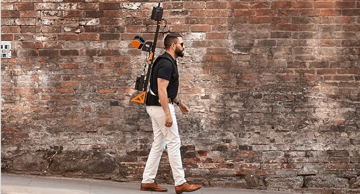 Man Walking and Carrying Scanning Equipment next to a Brick Wall