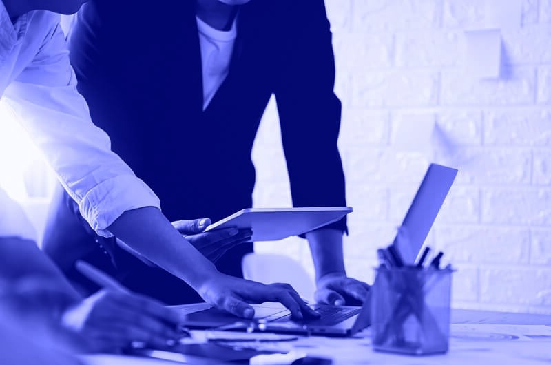 Blue Image of Two People Working on a Laptop and a Tablet