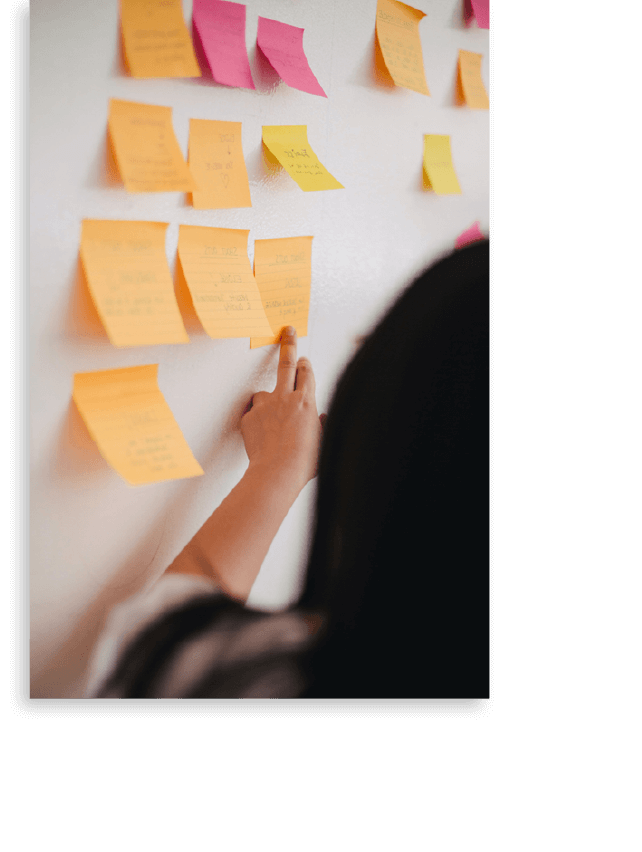 Woman Pointing at and Reading from Orange and Pink Post It Notes